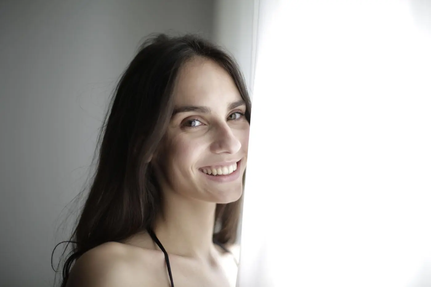Mujer sonriendo junto a una ventana con luz natural